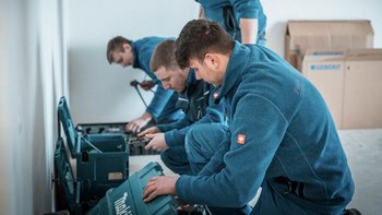 Vier Handwerker in blauen Arbeitsanzügen arbeiten konzentriert an einem Projekt, während sie Werkzeuge aus Kisten entnehmen.