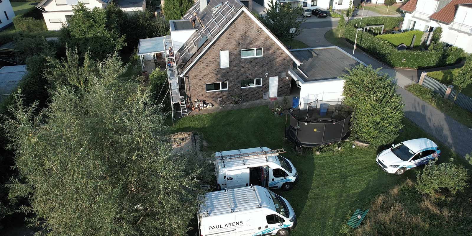 Eine Luftaufnahme eines Hauses mit Solarpanelen, umgeben von Bäumen und einem gepflegten Garten mit Spielgeräten.