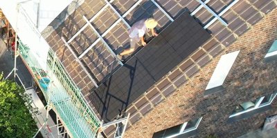 Der Arbeiter auf dem Dach trägt einen Hut und arbeitet konzentriert an der Montage von Solarpanels auf Ziegeln.