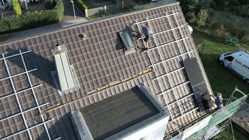 Ein Handwerker arbeitet auf einem Dach, während er eine Solaranlage installiert, umgeben von einem grünen Garten.
