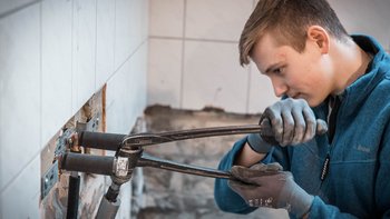 Ein junger Handwerker arbeitet konzentriert an einer Wand, während er eine Rohrzange benutzt, um Rohre zu befestigen.
