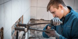 Ein junger Handwerker arbeitet konzentriert an einer Wand, während er eine Rohrzange benutzt, um Rohre zu befestigen.