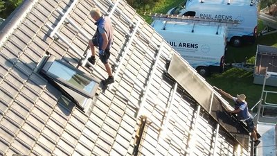 Auf dem Dach sind zwei Männer zu sehen, die an der Installation von Fenstern und Dachplatten arbeiten, um die Struktur zu verbessern.