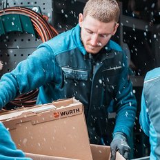 Drei Männer in blauen Arbeitsjacken laden einen Karton aus einem Lieferwagen, während es schneit.