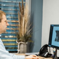 Ein Mann sitzt an einem Schreibtisch und schaut konzentriert auf zwei Computerbildschirme, während er an einem Projekt arbeitet.