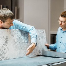 Zwei Männer in blauen Hemden betrachten Fliesenmuster in einem modernen Ausstellungsraum, einer zeigt auf ein Detail.