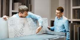 Zwei Männer in blauen Hemden betrachten Fliesenmuster in einem modernen Ausstellungsraum, einer zeigt auf ein Detail.